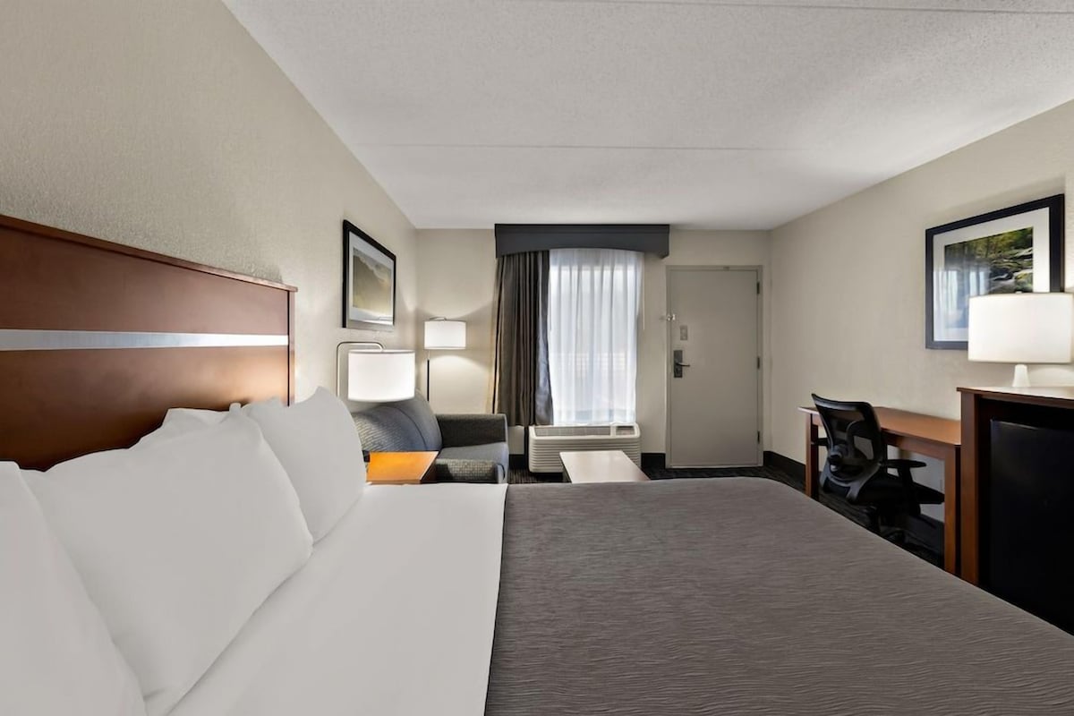 A hotel room with a large bed, a desk, a chair, a lamp, and a window with curtains.