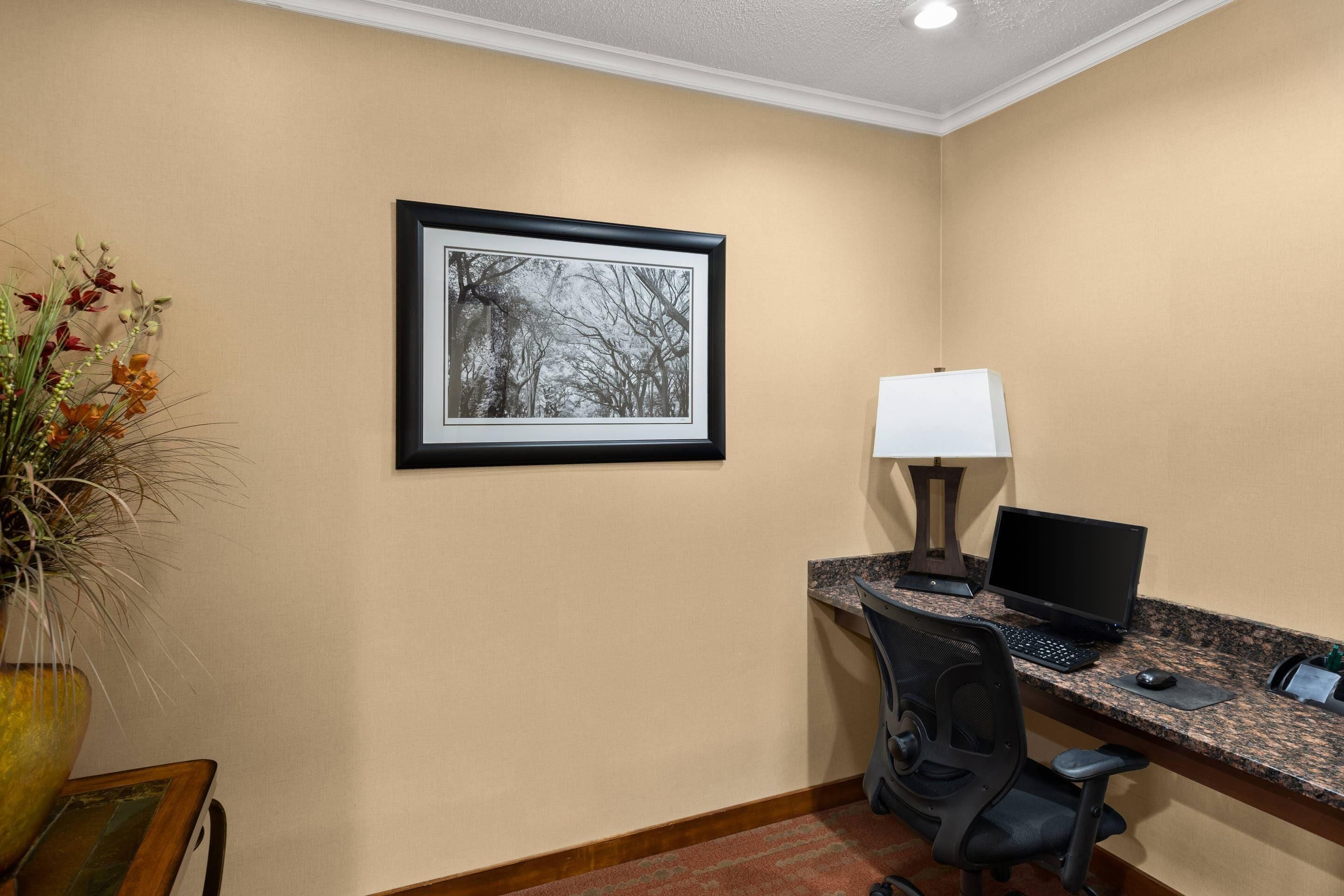 Une chambre d’hôtel équipée d’un bureau, d’un ordinateur, d’une chaise et d’un tableau encadré au mur.