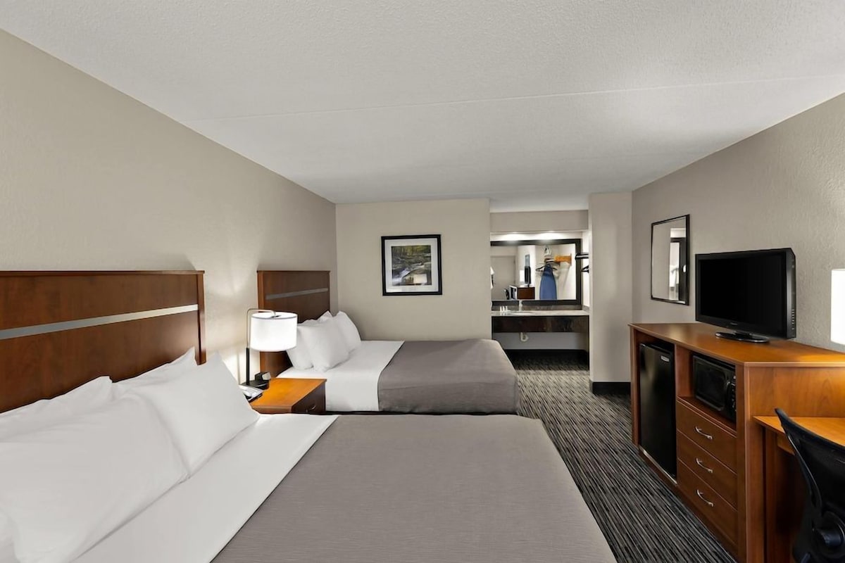 A hotel room with two beds, a desk, a television, and a bathroom visible in the background.