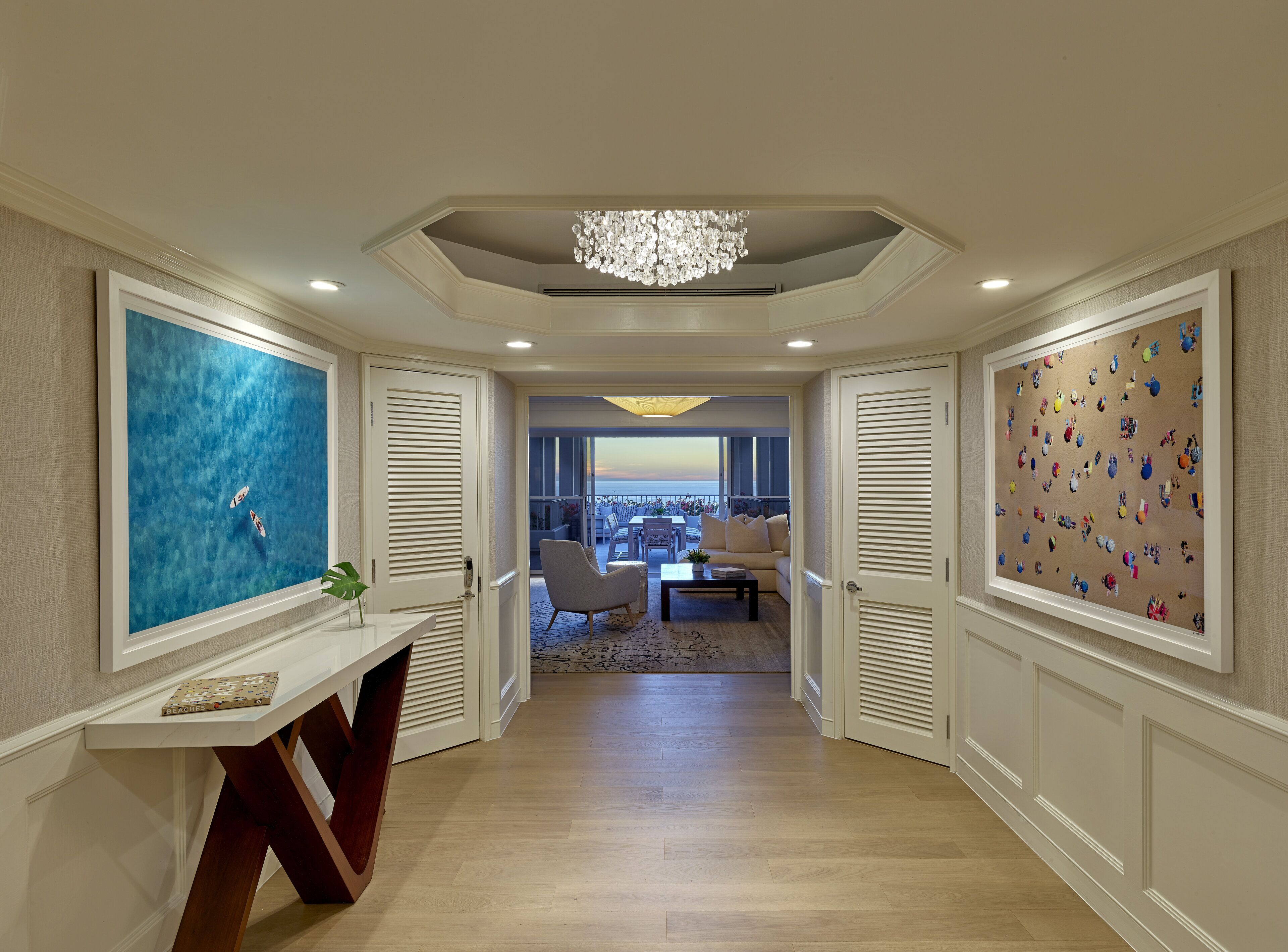 A hallway with a view to a balcony, a chandelier, and artwork on the walls.