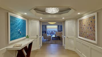 A hallway with a view to a balcony, a chandelier, and artwork on the walls.