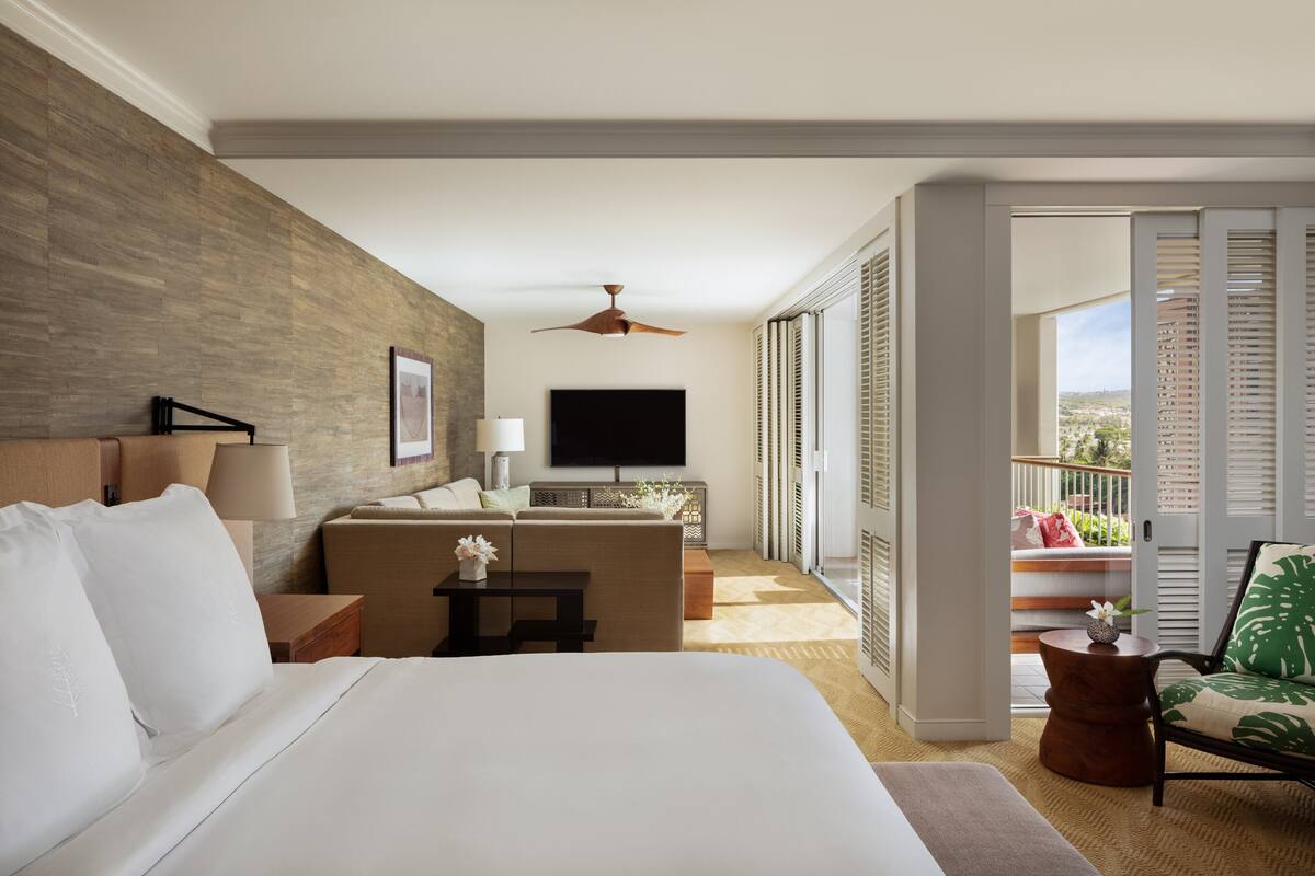 Ein Hotelzimmer mit einem großen Bett, einem Schreibtisch, einem Flachbildfernseher, einem Deckenventilator und einem Balkon mit Blick.