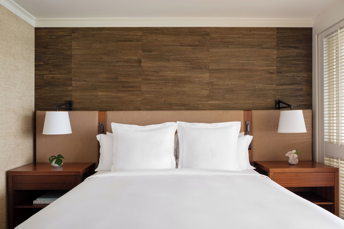 Una cama bien tendida con sábanas blancas, dos mesitas de noche con lámparas y un cabecero de madera.
