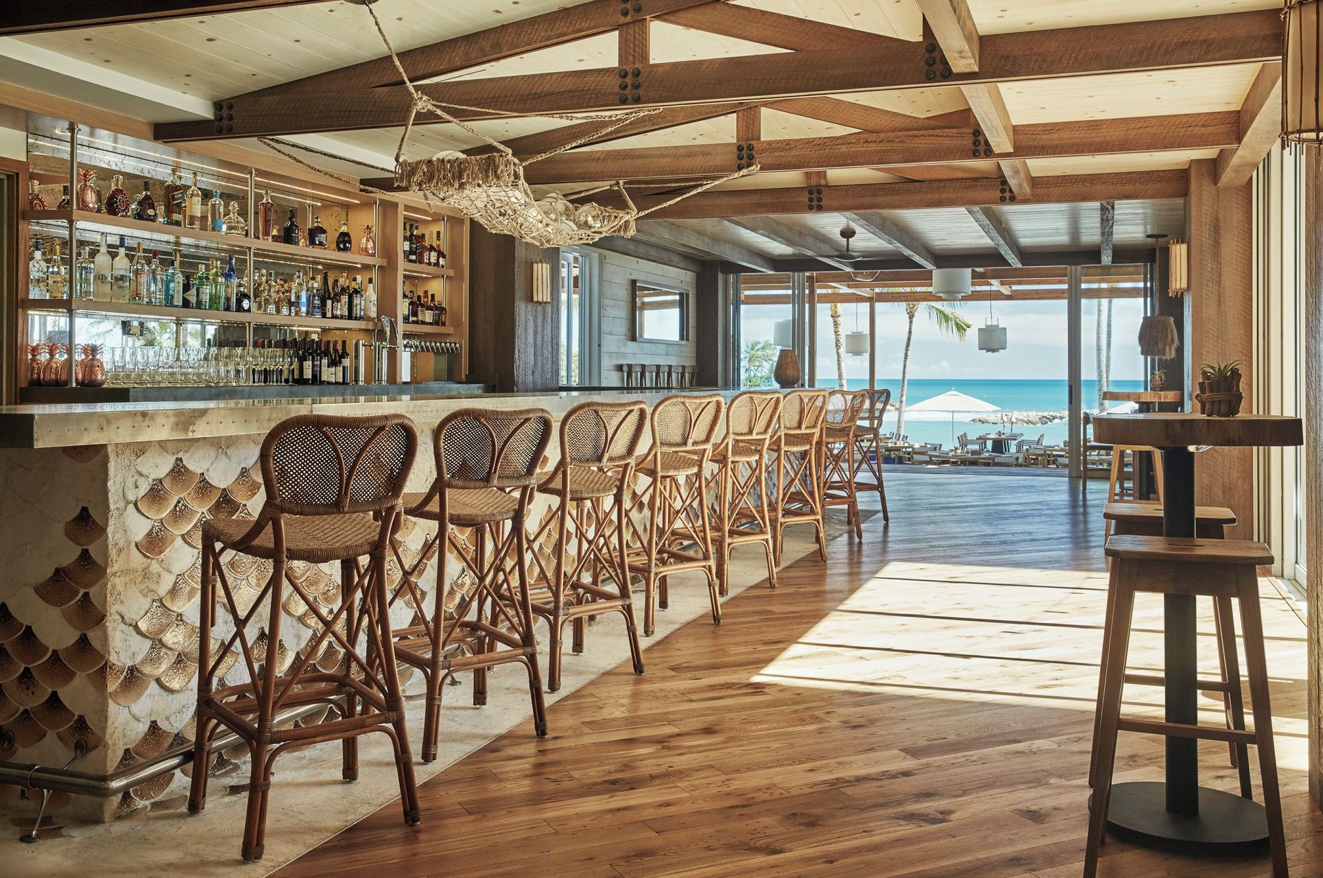 A bar area with wicker chairs, a wooden bar counter, and a view of the ocean.