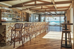 Zona de bar con sillas de mimbre, mostrador de bar de madera y vista al océano.