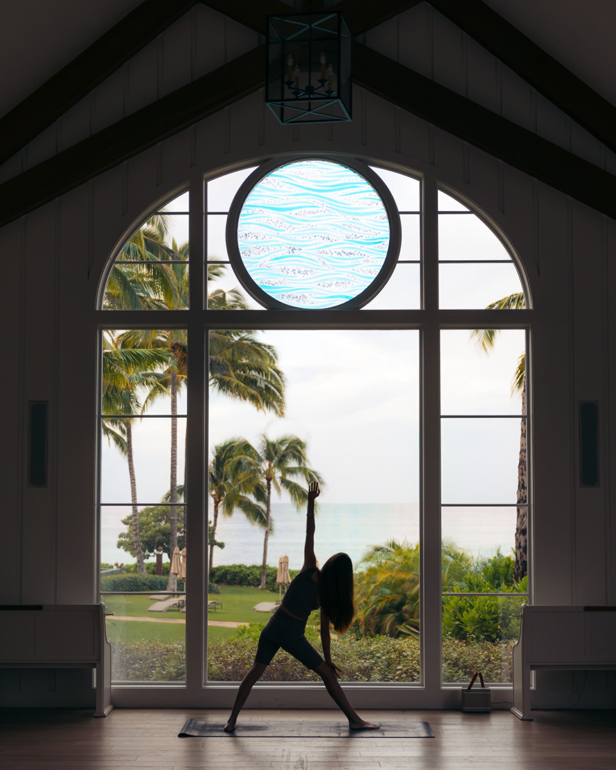 Una habitación con ventanas arqueadas amplias que dan a un paisaje tropical, con palmeras y vistas al océano.