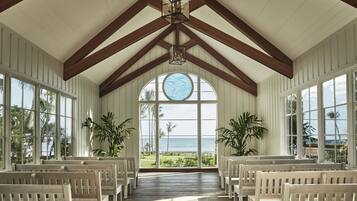 A room with wooden benches arranged in rows, large windows with a view of the ocean, and a circular skylight.