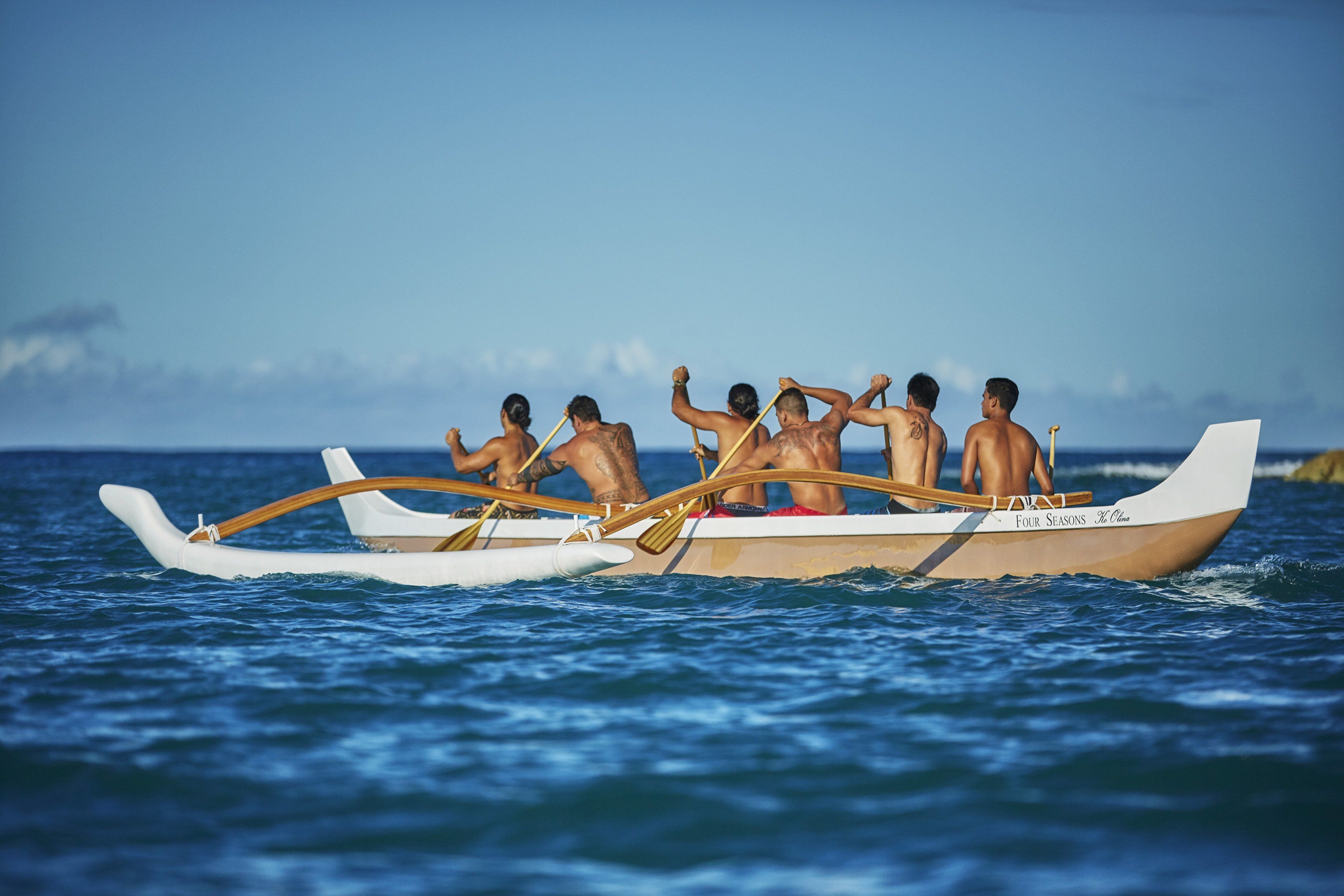 A boat with several people rowing, on a body of water.