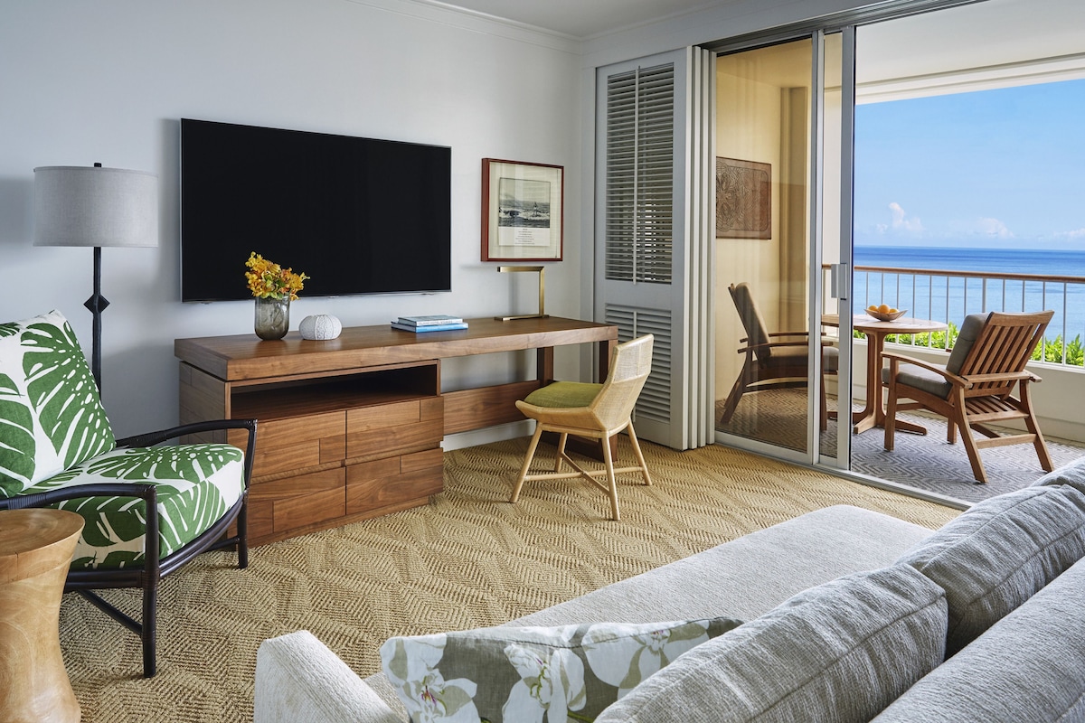Una habitación de hotel moderna con balcón, televisión de pantalla plana, escritorio de madera y sofá.