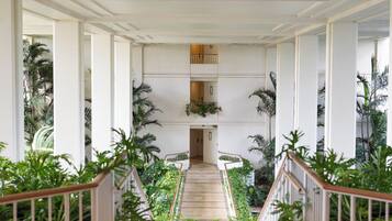 Un magnifique escalier à balustrades blanches, bordé d’une végétation luxuriante et de palmiers, mène à un palier situé au deuxième étage.