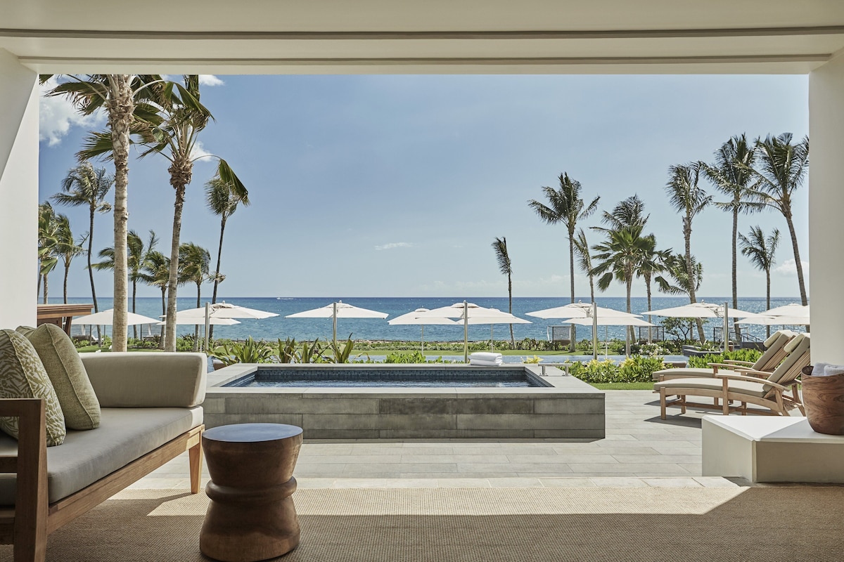 Un espacio moderno al aire libre con piscina, palmeras y vistas al océano.