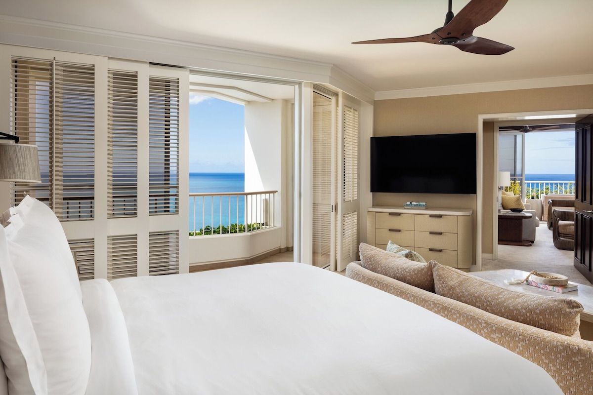 Habitación de hotel con cama, televisor, balcón y vista al océano, además de ventilador de techo.