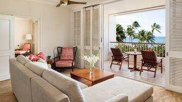A living room with a sofa, chairs, a coffee table, and a view of the ocean through a sliding door.