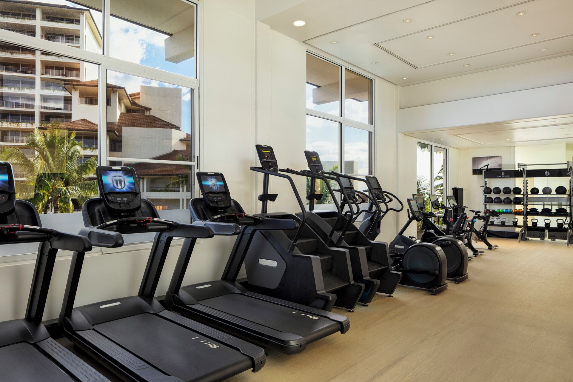 A gym with multiple treadmills and exercise bikes, large windows, and a view of a building outside.
