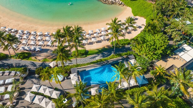 Vue aérienne d’un complexe hôtelier doté d’une plage, d’une piscine et de nombreux parasols.