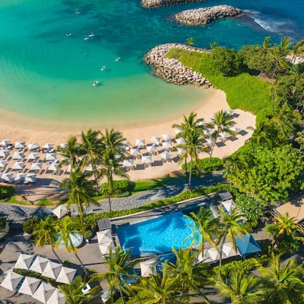 An aerial view of a resort with a beach, a swimming pool, and numerous umbrellas.