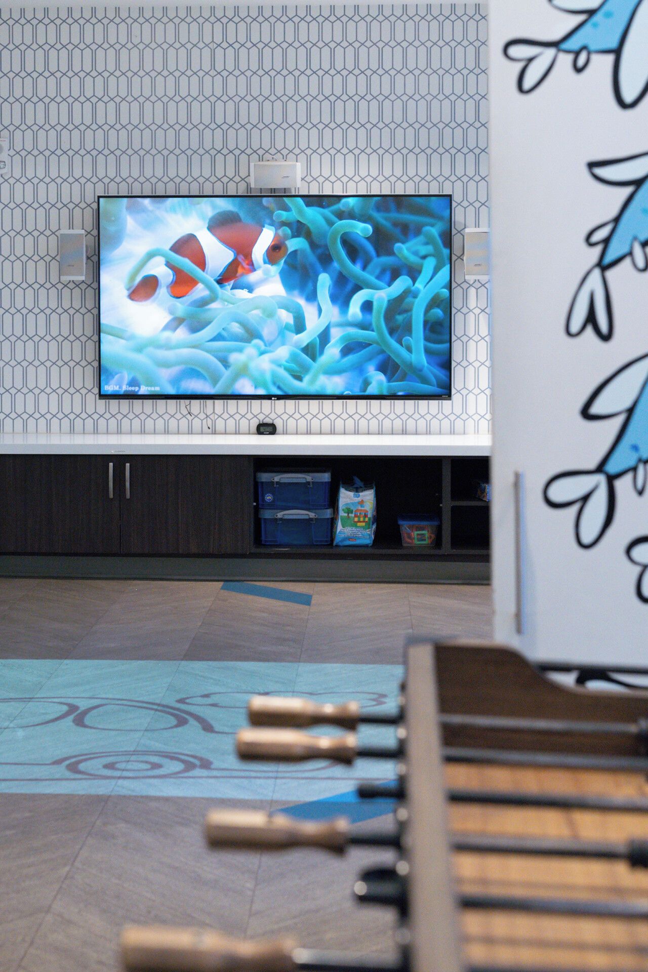Un televisor montado en una pared con un diseño geométrico, un mueble de almacenamiento debajo y un piso con diseño decorativo.