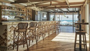 Un espace bar avec des meubles en bois, un comptoir bien garni de bouteilles et une vue sur l’océan.