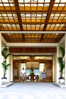 Entrada de hotel con techo de madera y grandes plantas en macetas.