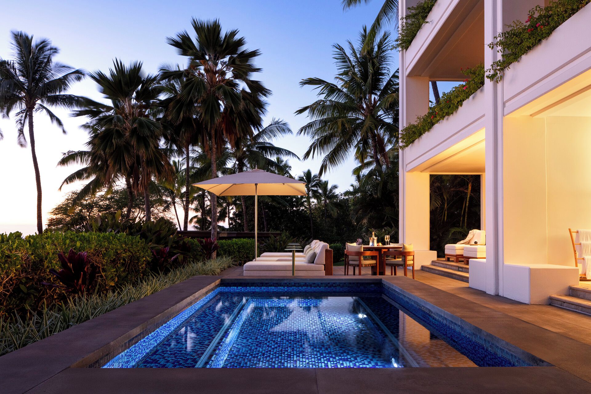 A modern outdoor pool area with a tiled design, surrounded by lush greenery and palm trees.