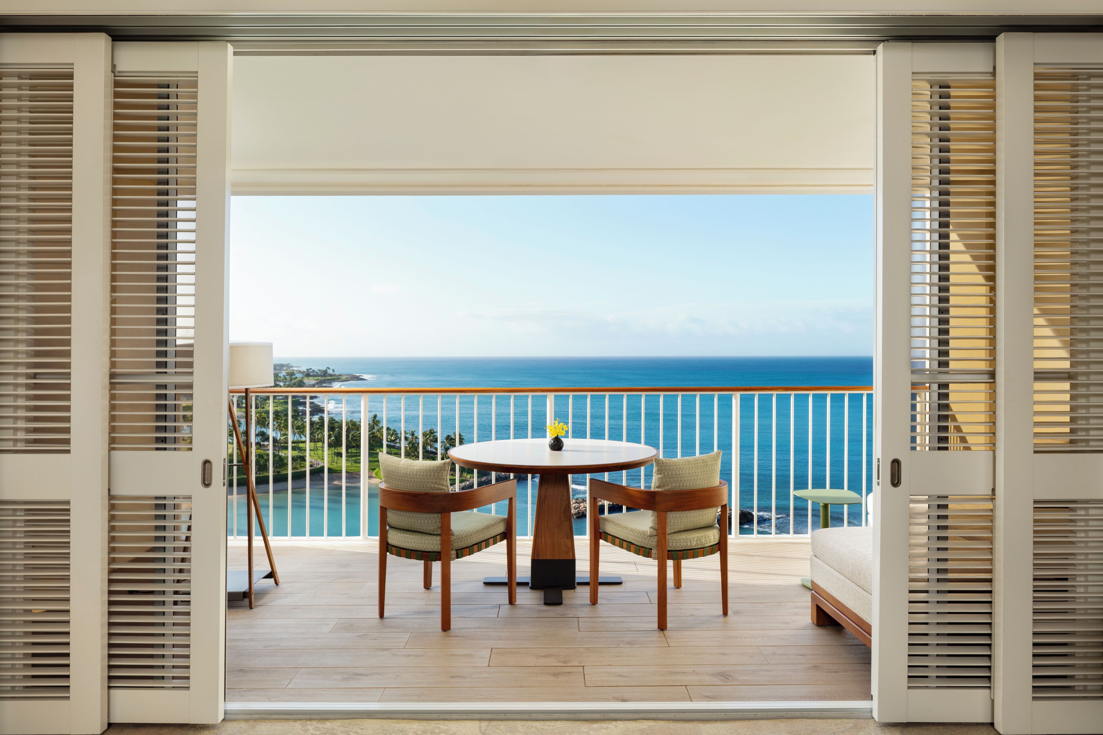 An open balcony with a wooden table and chairs, a view of the ocean, and a railing.