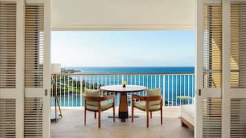 An open balcony with a wooden table and chairs, a view of the ocean, and a railing.