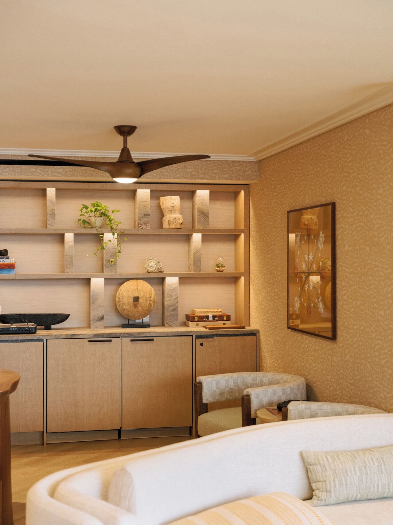 A modern interior with a sofa, a dining area with a ceiling fan, and a wall-mounted shelf with decorative items.
