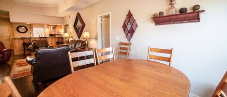 A dining area with a round wooden table and six chairs, a kitchen in the background, and decorative wall art.