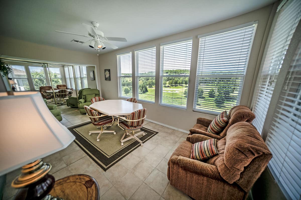 A spacious living room with a large window, a ceiling fan, and a dining area with chairs and a table.