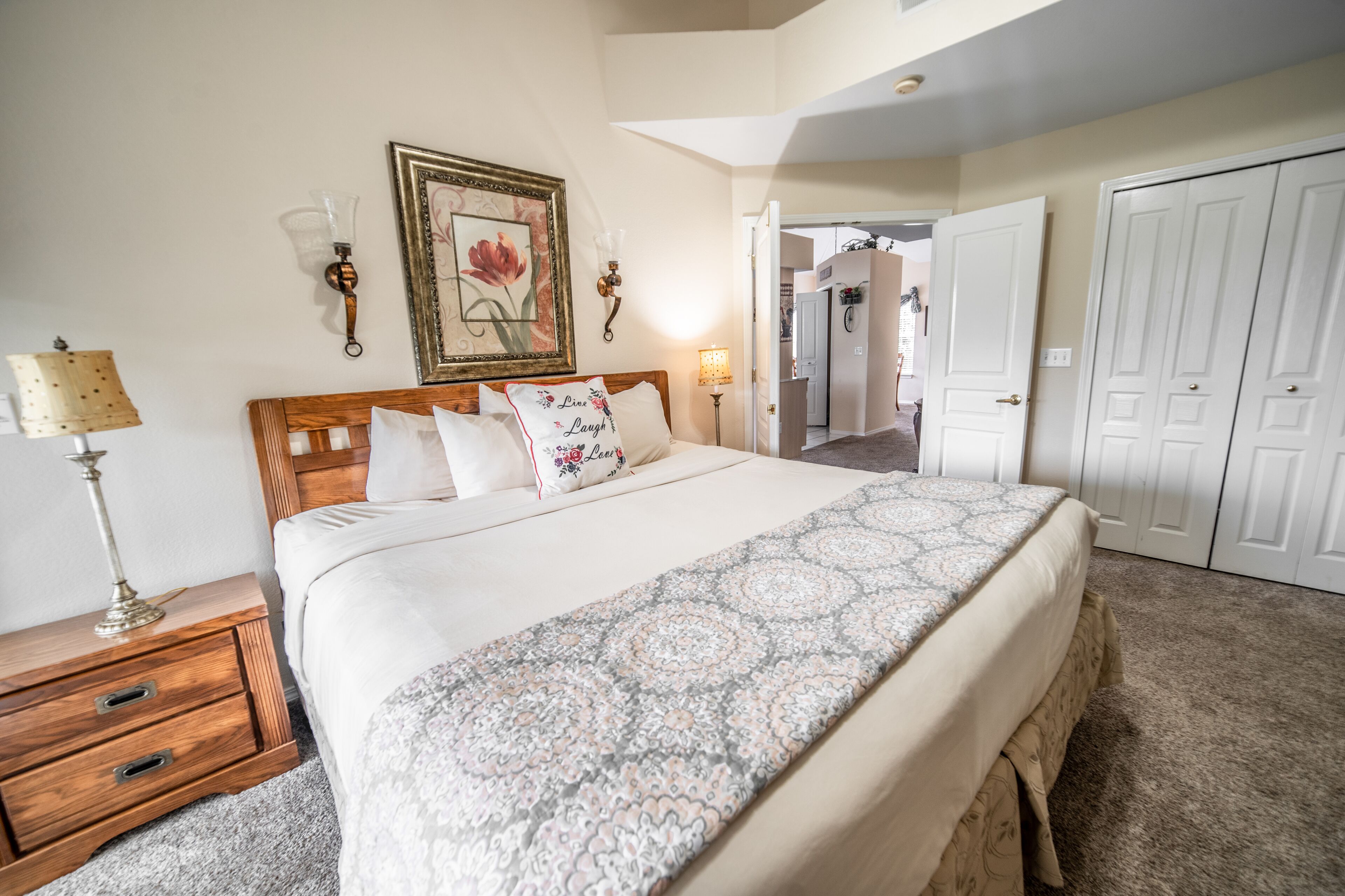 Un dormitorio ordenado con una cama grande, lámparas de noche, una obra de arte floral enmarcada y un armario.