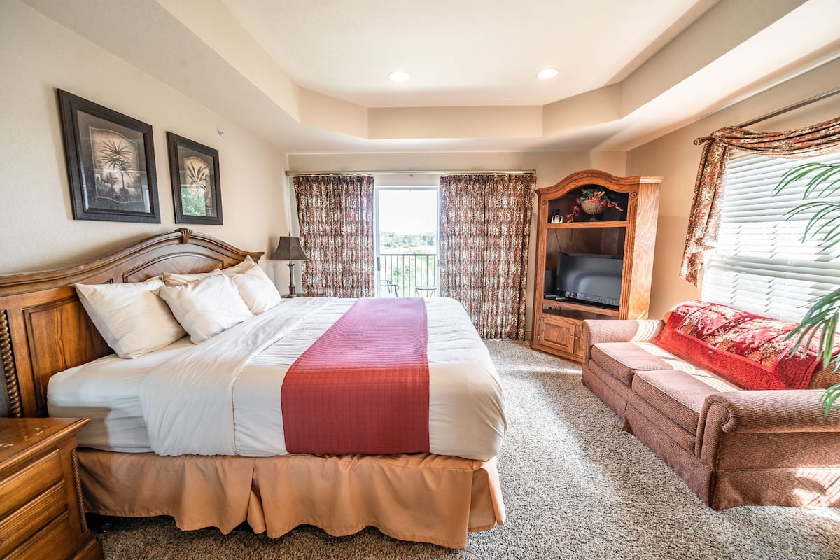 A bedroom with a large bed, a TV, a sofa, and a balcony view.