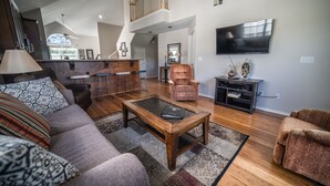 A spacious living room with a high ceiling, a large TV, and a kitchen area with a bar. - Thousand Hills Golf Resort (Branson)