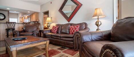 A living room with a brown leather sofa, a wooden coffee table, and a patterned rug.