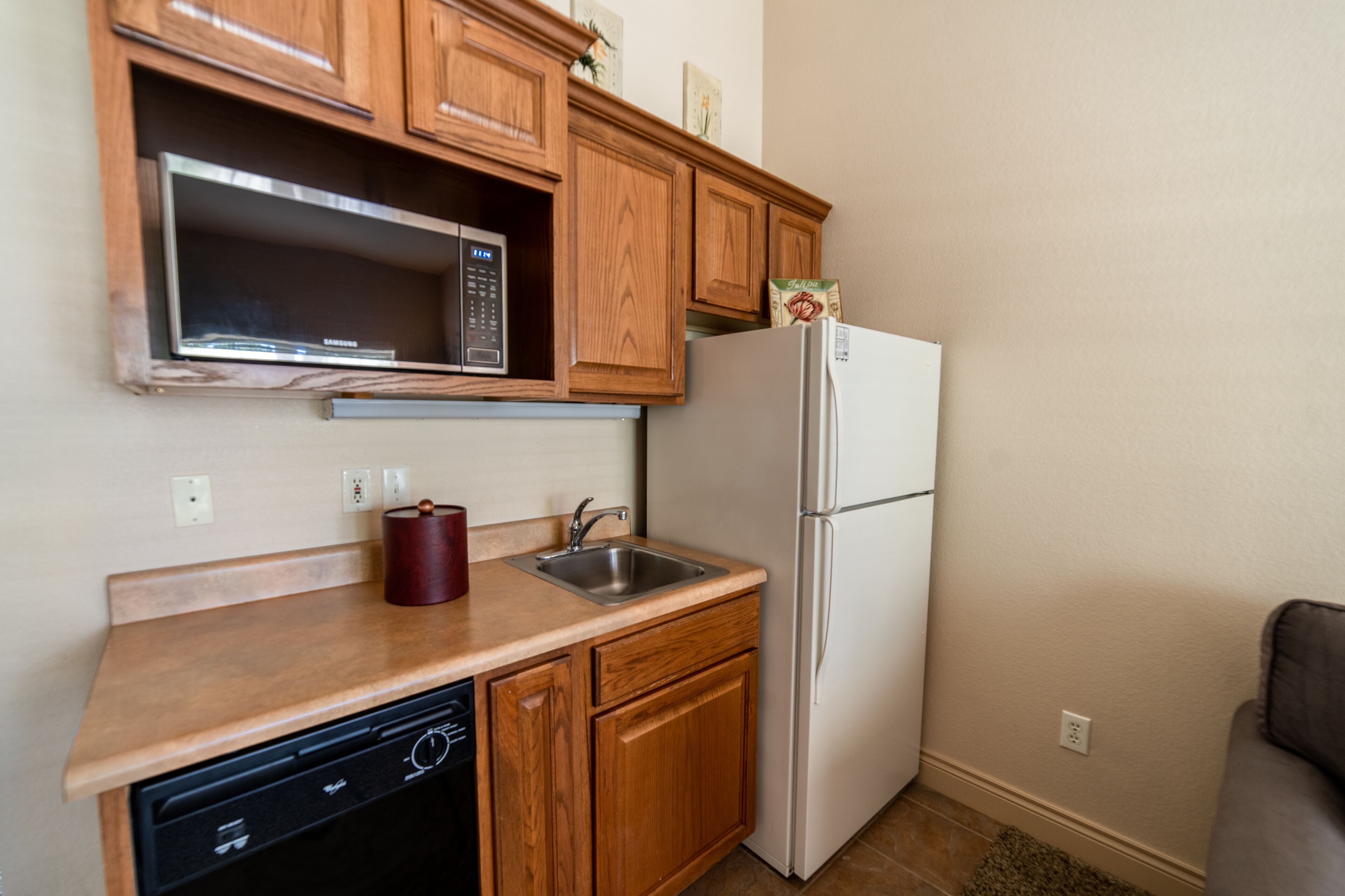 A compact kitchen with wooden cabinets, a microwave, a sink, a dishwasher, and a refrigerator.