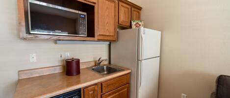 A compact kitchen with wooden cabinets, a microwave, a sink, a dishwasher, and a refrigerator.