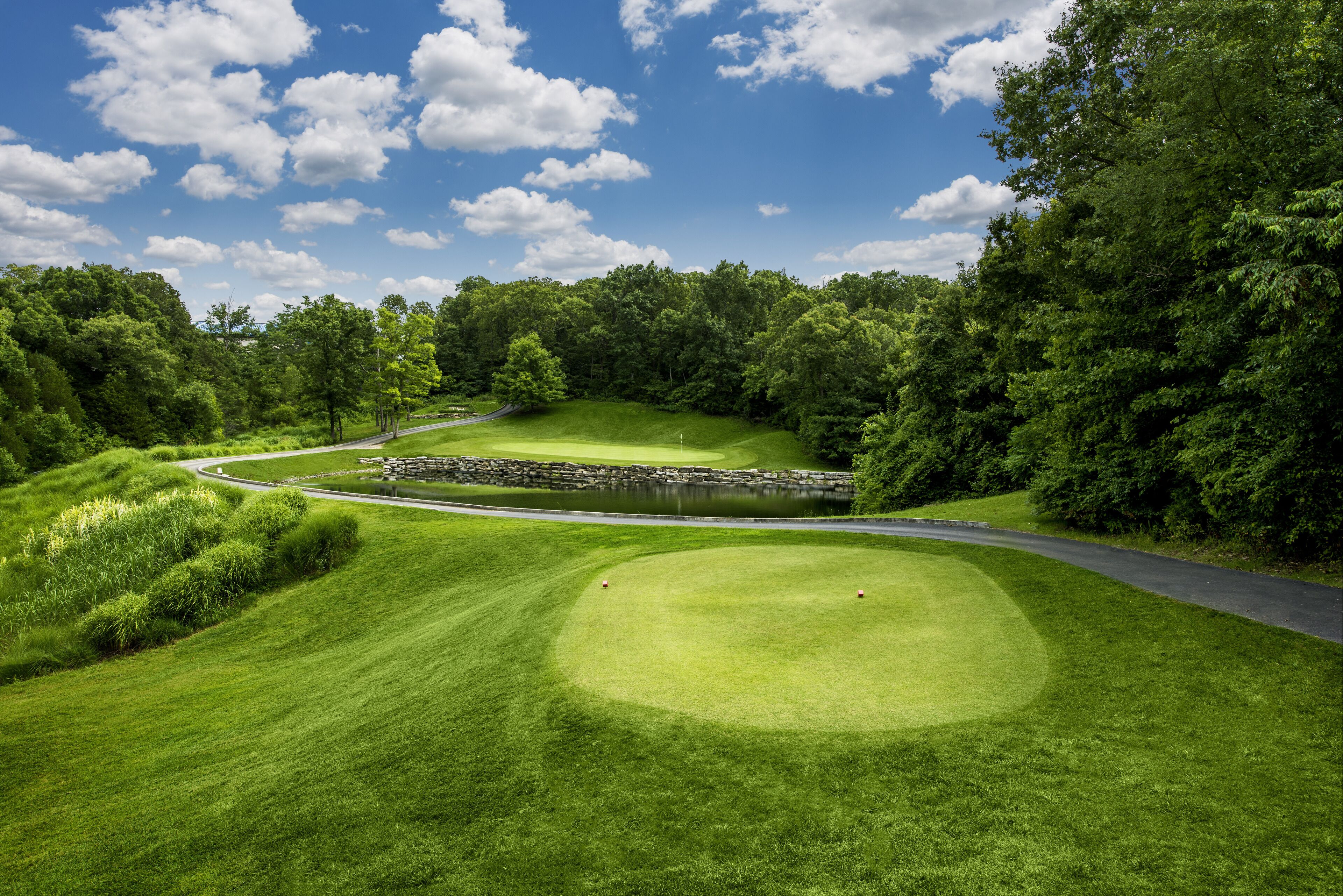 A golf course with a stone bridge, lush greenery, and a clear blue sky.