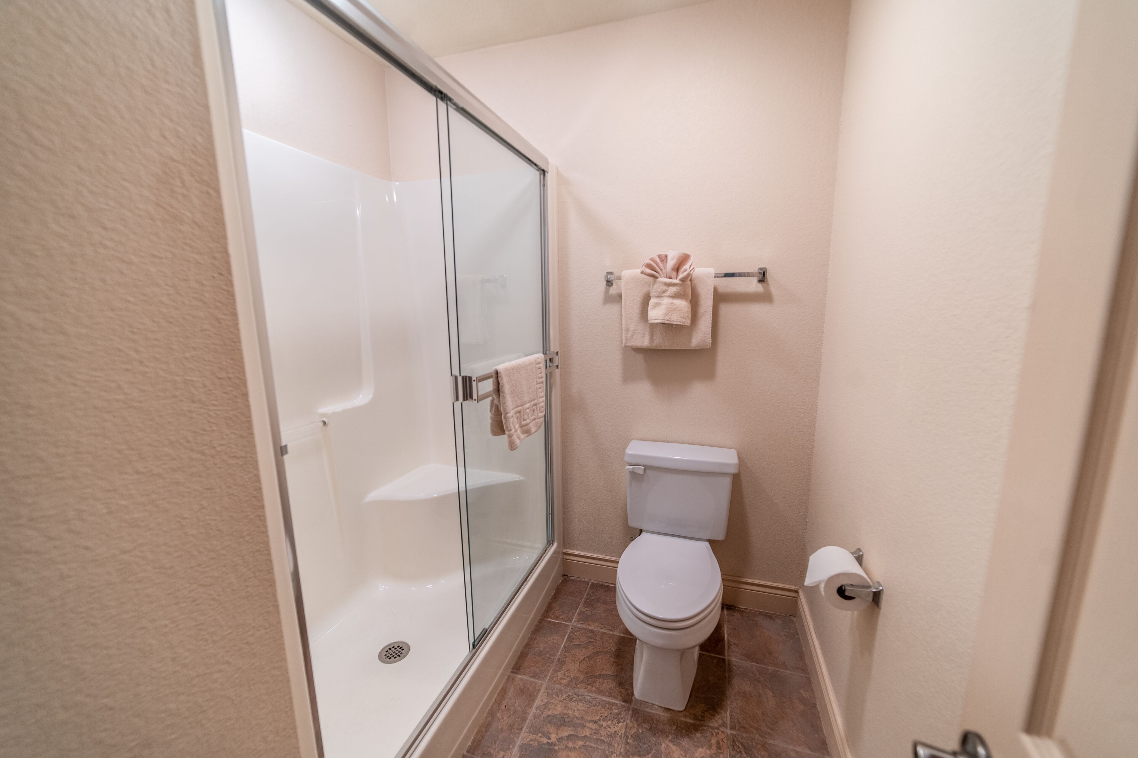 A bathroom with a glass-enclosed shower, a toilet, and a towel rack with towels.