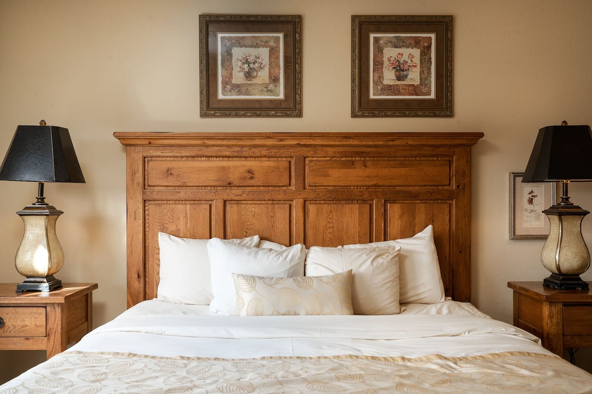 A neatly made bed with white linens and a wooden headboard. There are two framed pictures on the wall above the bed.