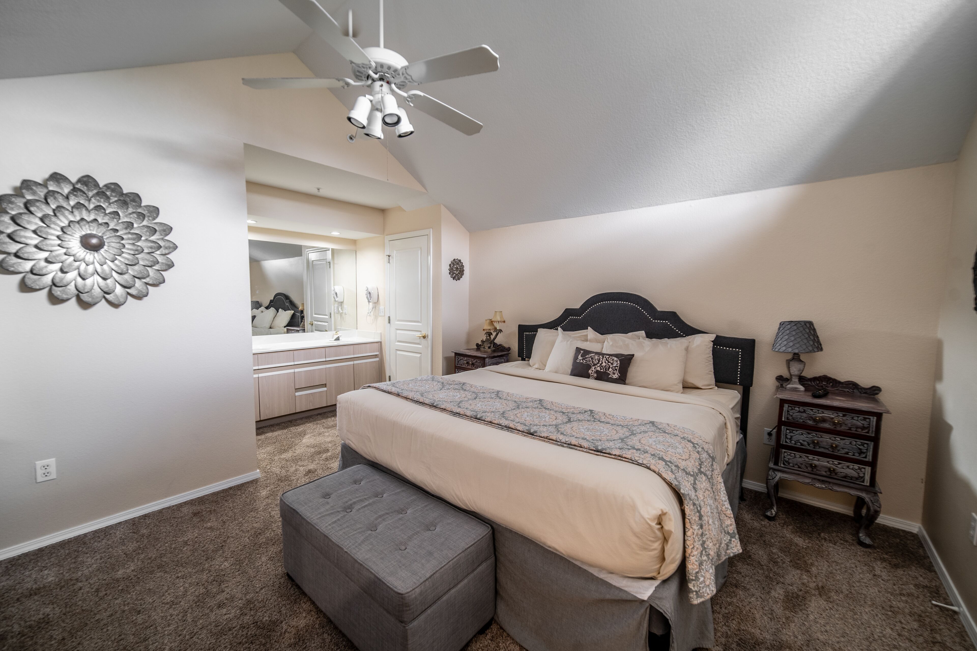 A bedroom with a bed, a vanity, a dresser, a nightstand, and a ceiling fan.
