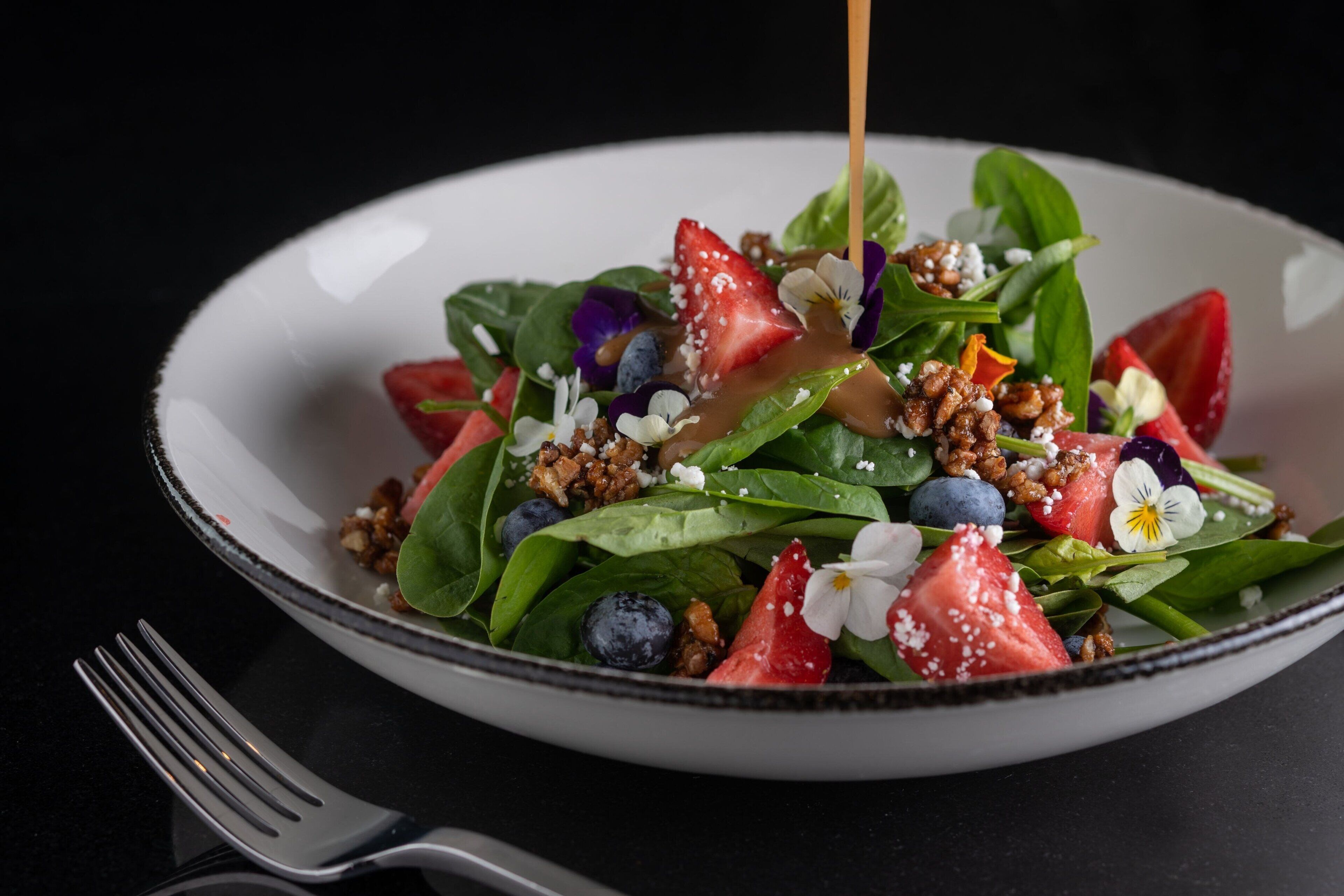 Une assiette blanche contenant une salade composée de fraises, de myrtilles et de noix, avec une fourchette à côté.