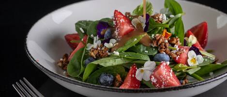 Un plato blanco con ensalada, incluyendo fresas, arándanos y nueces, con un tenedor a un lado.