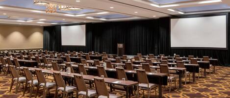 A conference room with rows of tables and chairs, large screens, and chandeliers.