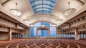 Un amplio hall de hotel con techo alto, ventanas grandes y alfombra estampada.