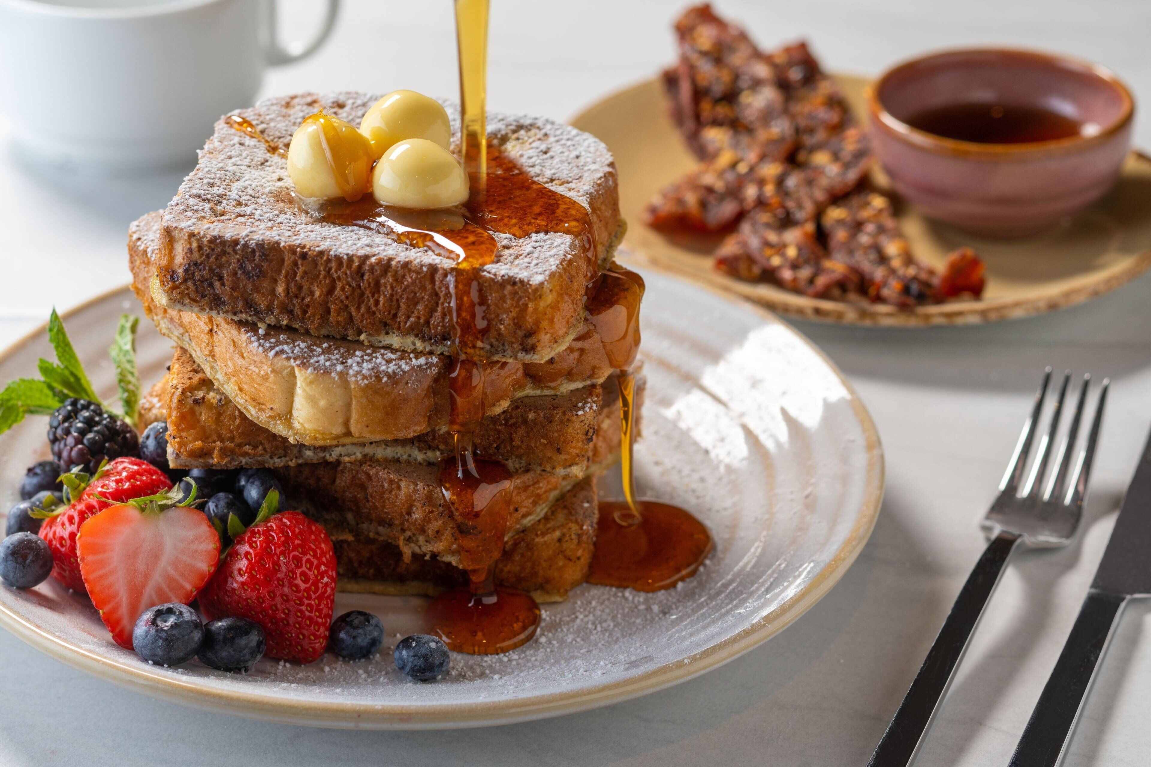 A breakfast plate with French toast, syrup, blueberries, and strawberries.