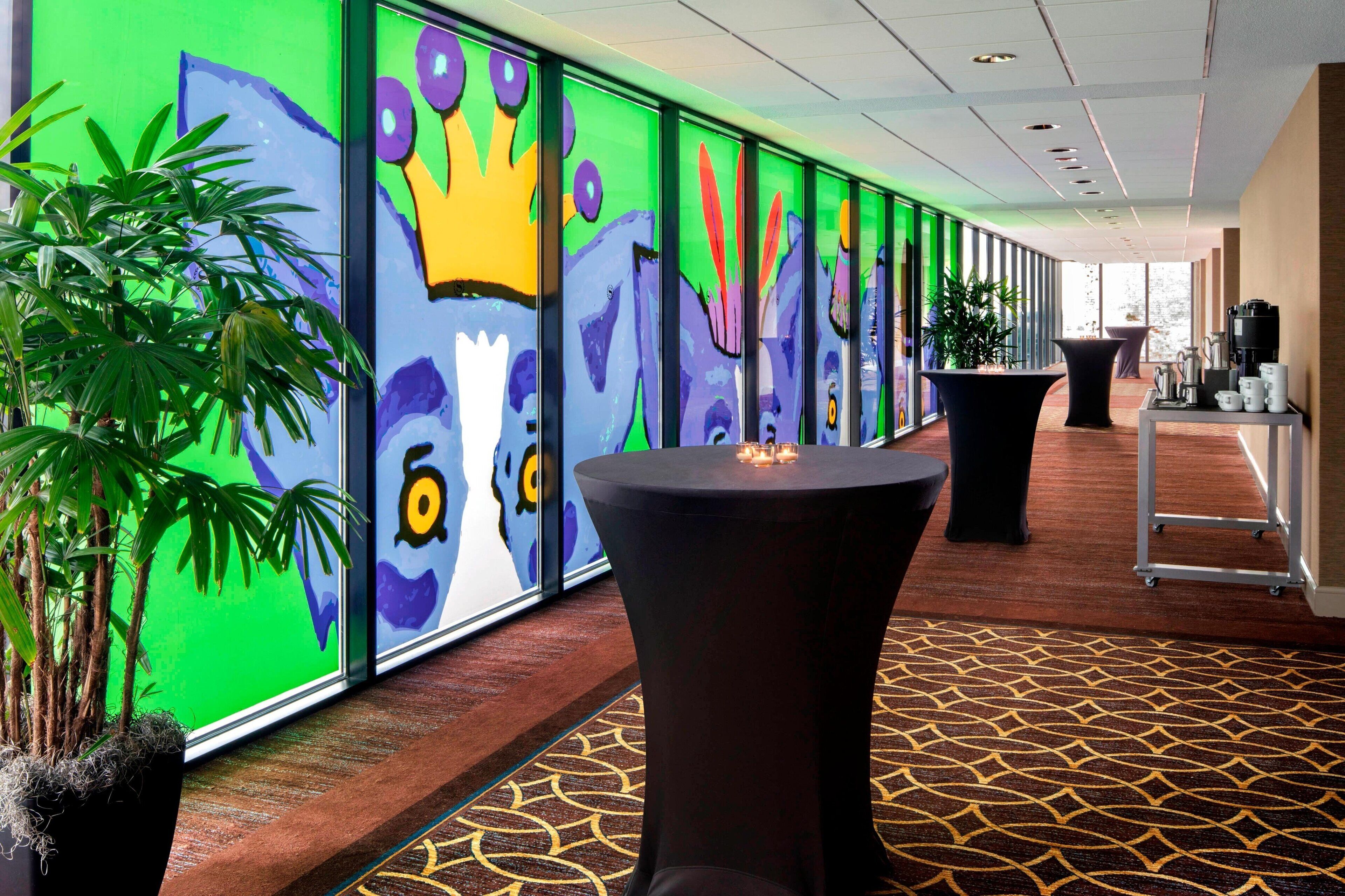 A hallway with colorful murals, a round table, and potted plants.
