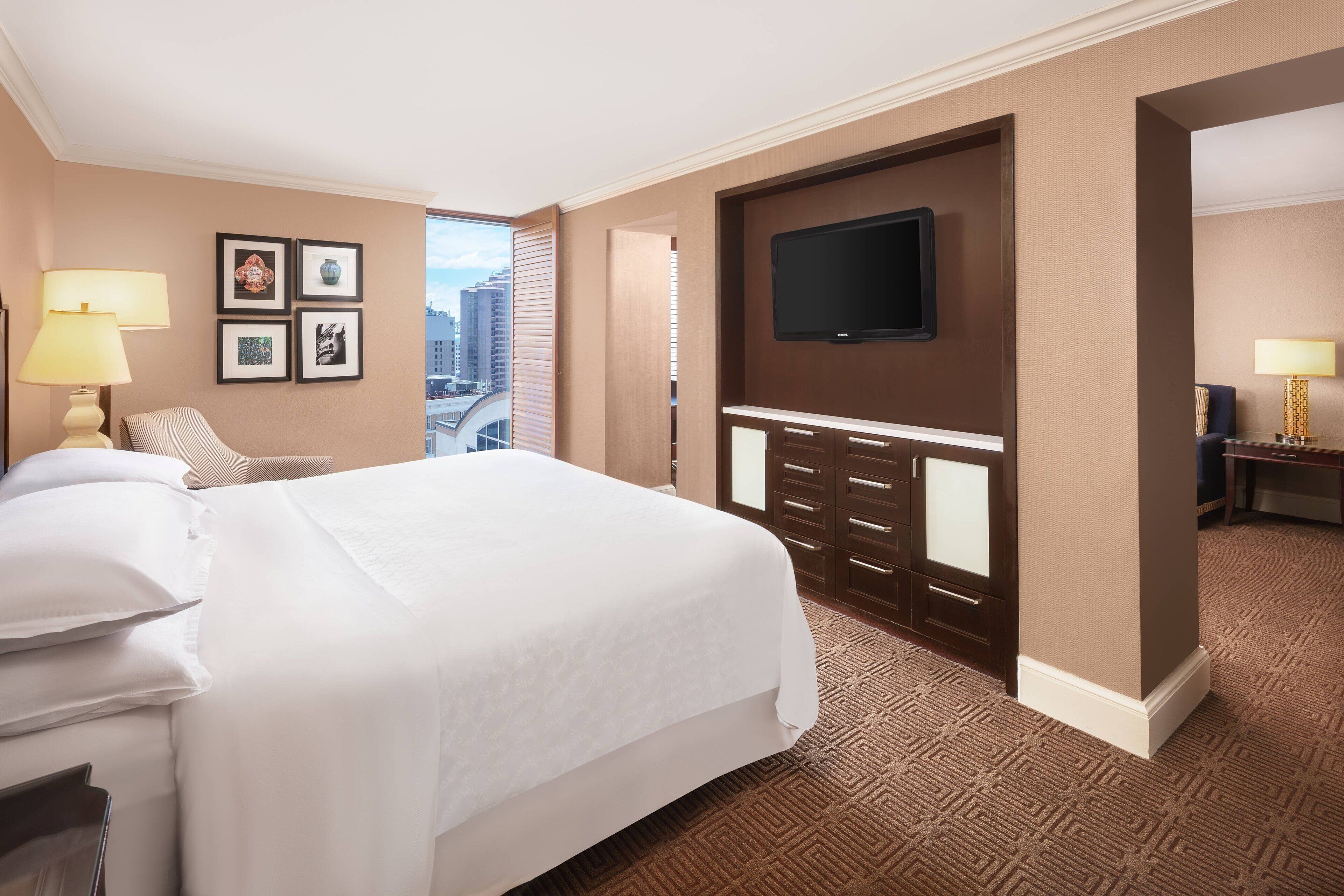 Hotelkamer met een groot bed, een flatscreen televisie aan de muur, een bureau met lamp en uitzicht op de stad.