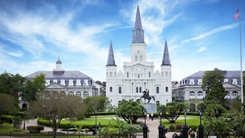 A large, historic building with three spires and a statue in front.