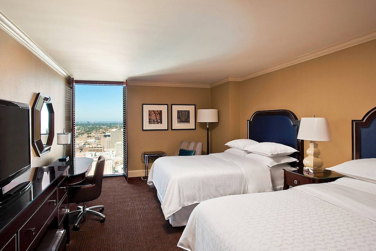 A hotel room with two beds, a desk, a chair, and a TV.