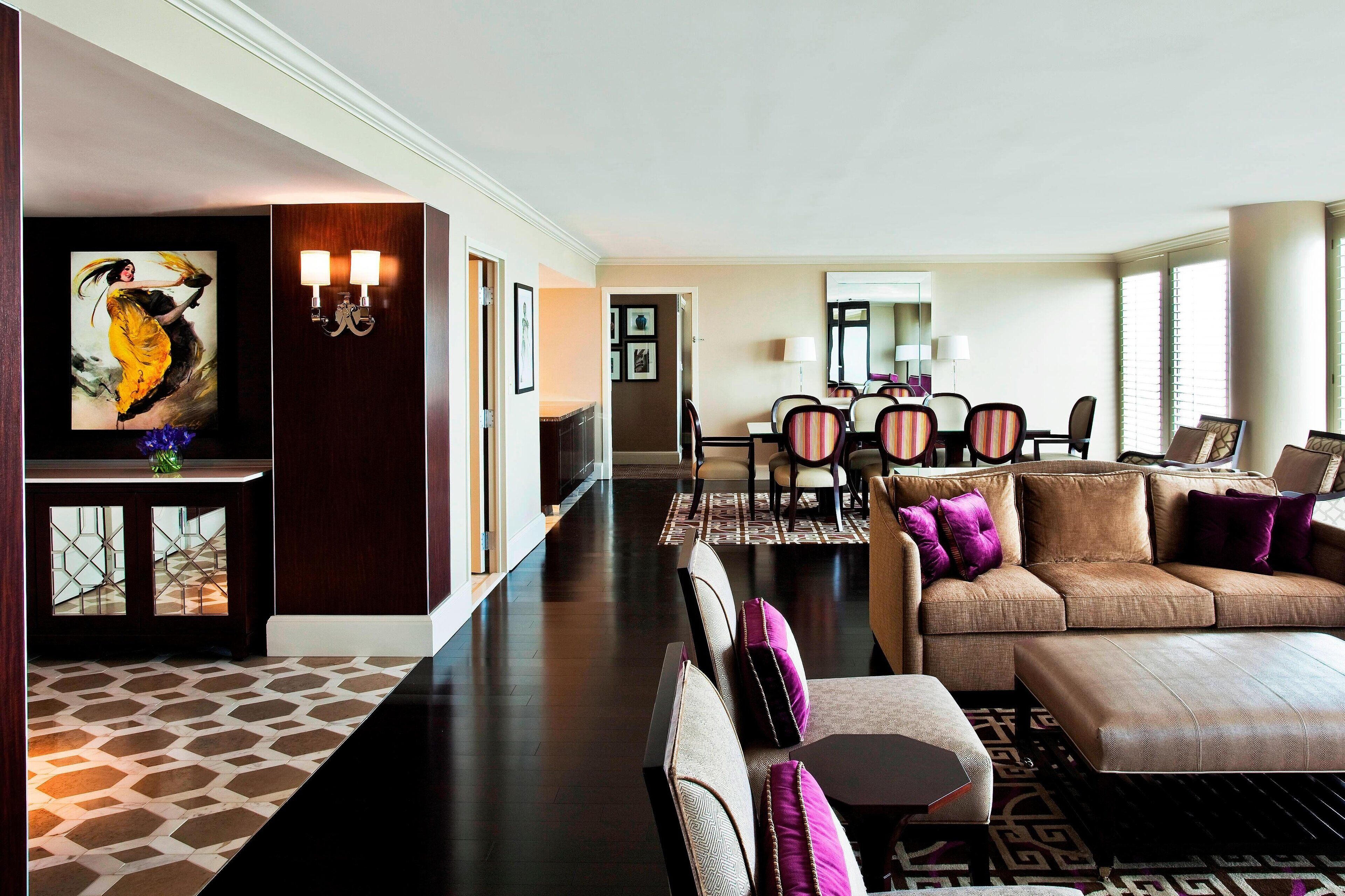 A spacious living area with a sofa set, a dining table, and a large painting on the wall.
