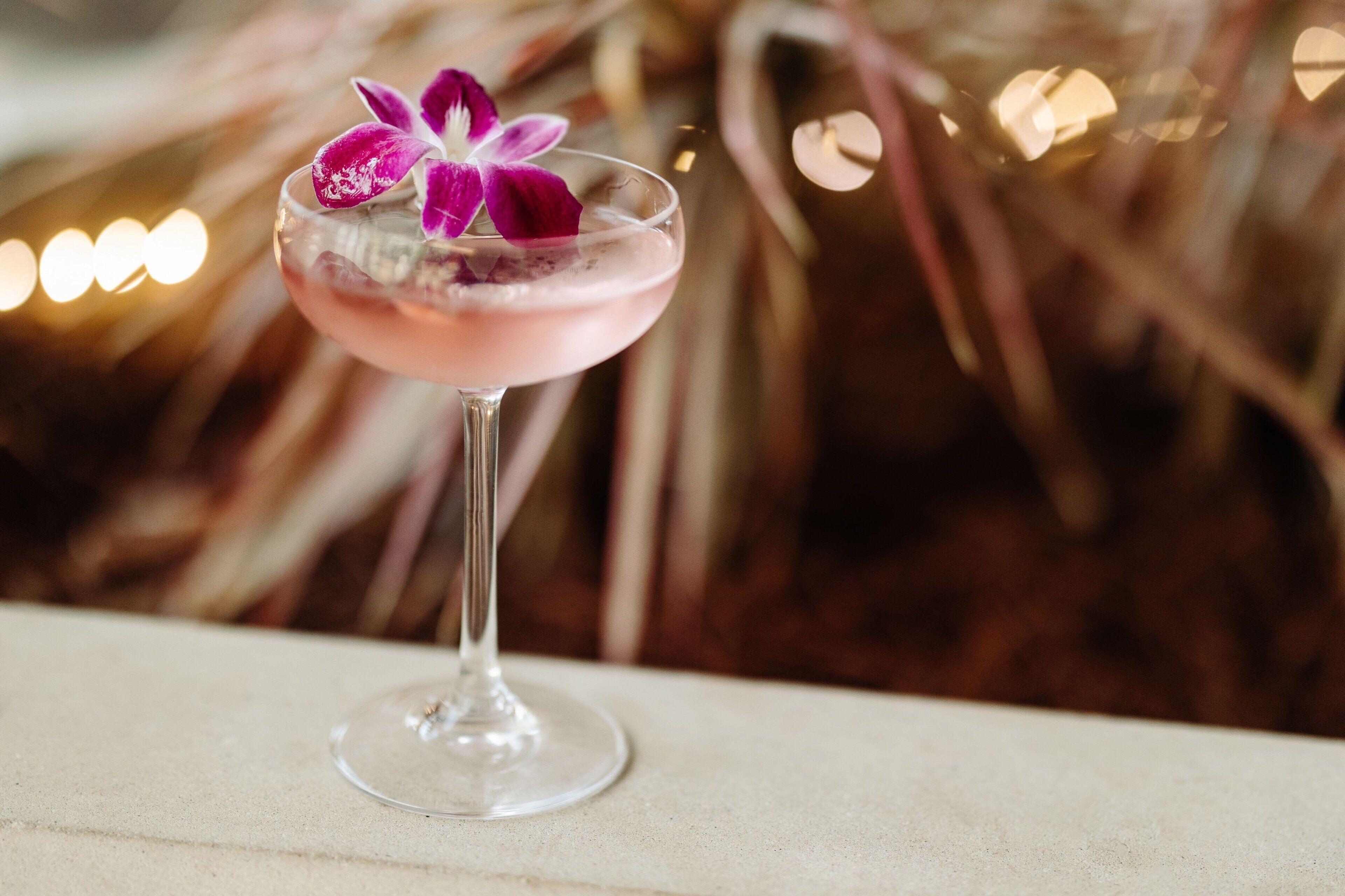 Un verre à cocktail contenant une boisson rose et une orchidée violette, posé sur une table.